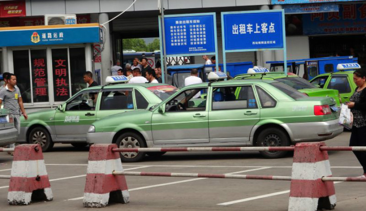 Chiny. Grupa taksówkarzy czekających przy bramie dworca autobusowego.